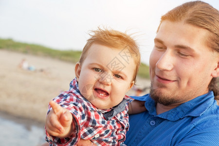 年轻父亲在海滩上抱着孩子有趣的表情玩得开心儿子和父母的亲情图片