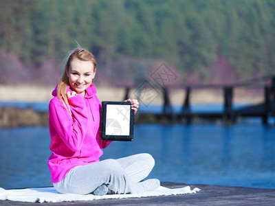 身穿粉色运动服的健身女少全年都在户外码头上摆放的平板触摸电脑空白间屏幕图片
