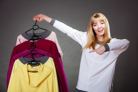 抗震支吊架零售和销金发美女时装服顾客与衣着多彩灰色背景的手指衣架