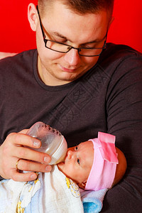 快乐的年轻父亲在家沙发上用奶瓶喂新生女婴图片