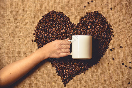 在咖啡豆心脏对面拿着白杯子的人图片
