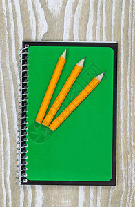 办公室桌面上有三支铅笔上面有旧白木的笔记板顶端角度以垂直格式拍摄图片