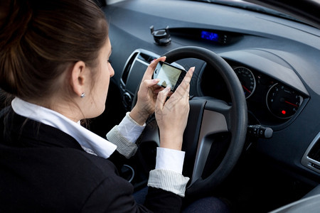 青年女商人驾驶汽车时使用智能手机图片