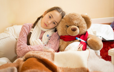 悲哀感冒躺在床上与泰迪熊躺在床上的女孩肖像图片