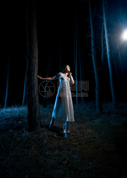 穿着白睡衣的单身女人看着夜林的光束图片