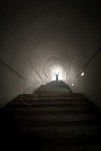 站在隧道尽头的灯光束上举起双手的人概念照片图片