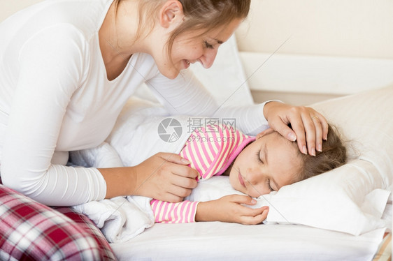 微笑的年轻母亲用手握着睡的女儿头部肖像图片