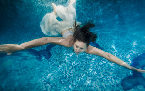穿白裙子的美丽黑发女在游泳池水下图片