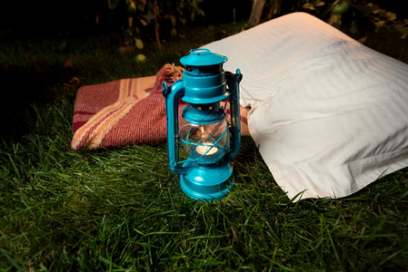 在枕头和毯子旁边草地上站立的旧油灯贴近镜头图片