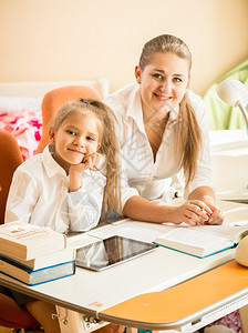 微笑的母亲和女儿坐在桌子上看镜头坐在桌子上看着镜头一副笑着的母亲和女儿肖像图片