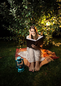 妇女晚上在花园灯光下阅读书时挨门外击图片