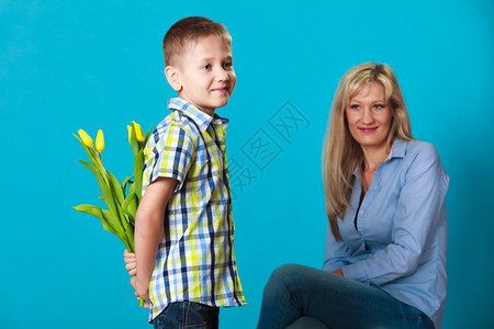 假日母亲概念背着一堆黄色的郁金香背着黄色郁金香的男孩后院观看准备给母亲工作室拍蓝色的惊喜图片