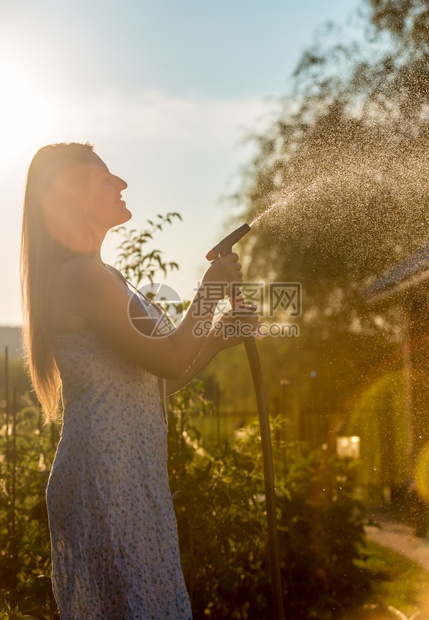 在阳光明媚的白天女人用水管浇灌花园的天空图片