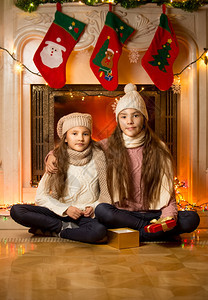 两个可爱女孩的肖像坐在旁边装饰的壁炉圣诞节图片