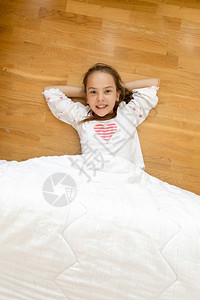 小笑的女孩被木地板上的毯子覆盖着图片
