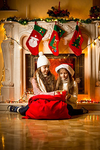坐在壁炉旁边的漂亮女孩看着Santa礼物图片