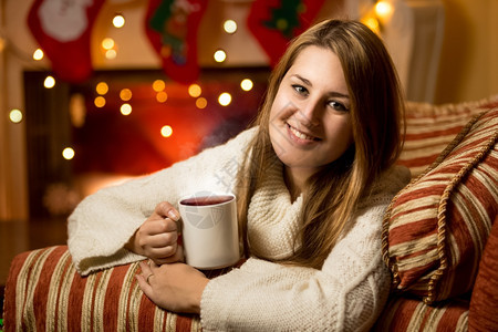 圣诞前夕在壁炉里喝着热茶的笑女人美丽肖像图片