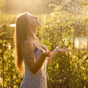 美丽的女人肖像在阳光明媚的白天在花园享受雨水图片