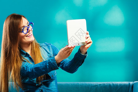 技术互联网现代生活方式概念女孩使用数字平板照相片自拍风格在沙发上用电子书阅读器触摸式Pc的妇女蓝色图片