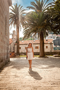 年轻优雅的女子在街上行走与古老建筑和高棕榈图片