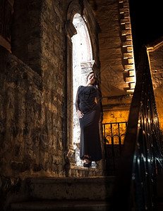 穿着长裙的感瘦女人晚上靠着旧石拱门图片