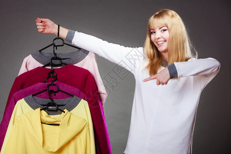 零售和销金发美女时装服顾客与衣着多彩灰色背景的手指衣架对着顾客