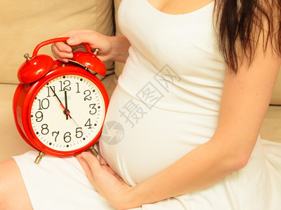孕妇拿着红色闹钟等待坐在沙发上图片