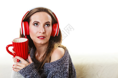 妇女随便的红色大耳机听音乐mp3坐在沙发上家休息喝热茶图片