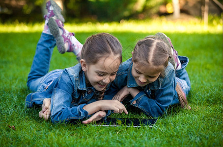两个小姐妹躺在绿草上玩石板图片
