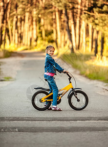 女孩在森林骑黄色自行车的照片图片