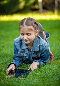 近距离拍摄的小女孩躺在草地上用平板电脑图片