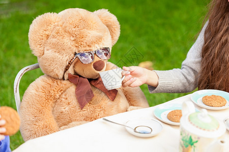 可爱的女孩在院子里给泰迪熊喝茶图片