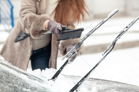 妇女从雪中用刷洗车擦器的近镜头图片