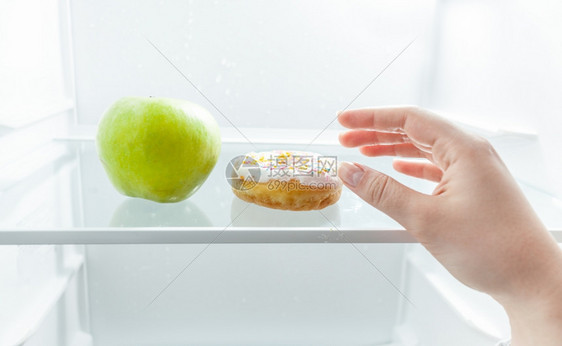 手在冰箱苹果和甜圈之间选择的剪切肖像图片