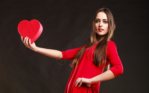 穿着红衣的年轻美女拿着心箱送礼物在工作室的灰色背景上图片