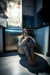 年轻女晚上在冰箱旁边吃饭的照片图片