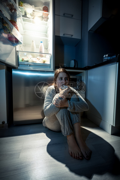 年轻女晚上在冰箱旁边吃饭的照片图片