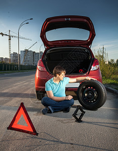 坐在路边靠着损坏汽车的年轻人图片