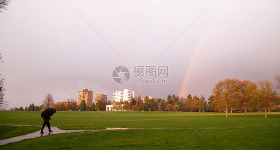 太阳升起一瞬间照亮了路的光芒并产生了一道彩虹靠近个带着雨伞走来的人图片