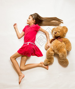 从躺在地上笑的女孩顶上被孤立的镜头假装跟泰迪熊跑得快图片