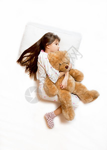 可爱女孩躺在床上拥抱泰迪熊的照片图片