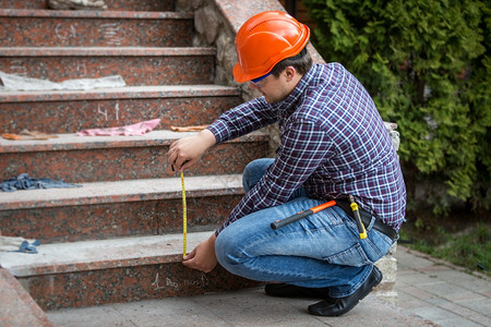 通过测量磁带检查楼梯高度的青年建筑工人图片