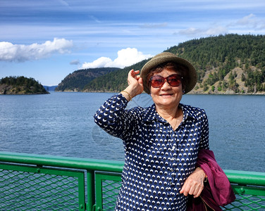 身穿帽子和太阳眼镜站在船对岸上背着海洋山顶和蓝天空的护栏图片