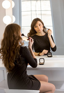 年轻优雅女人的肖像在镜子里化妆时用灯泡图片