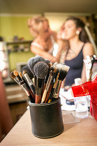 一组专业化妆刷的近视镜头与为年轻女化妆的艺术家相比图片
