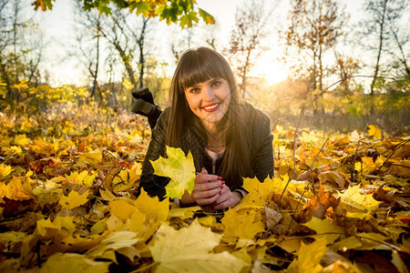 在秋天公园满树叶的地上躺着笑黑发女人图片