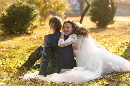 美丽的一对刚结婚夫妇在秋天公园的草地上放松图片
