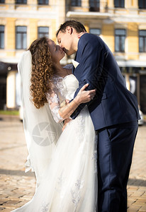 美丽的新娘和郎在阳光明媚的天在街上热情地接吻图片