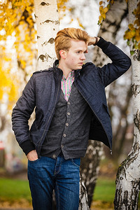 秋天季节和人的概念年轻时尚的男子肖像穿着格子衬衫和外套与秋天的白树对立图片