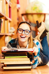在学校教育概念中穿着蓝眼镜的聪明女学生孩躺在大图书馆的地板上阅读书本图片